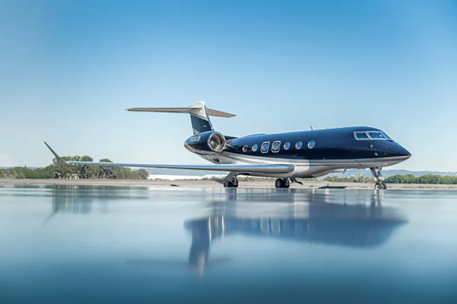 A dark blue and white Gulfstream G650 business jet, tail number N609JS, parked on a wet tarmac under a clear blue sky.