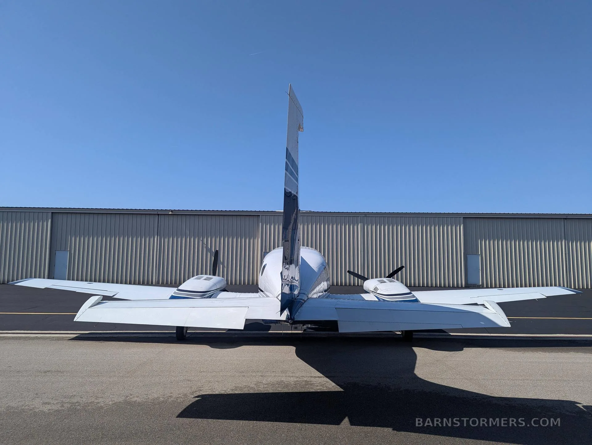 A rear view of a white and blue twin-engine propeller aircraft (Cessna 414 Chancellor) with tail number N533AC parked in front of a hangar.