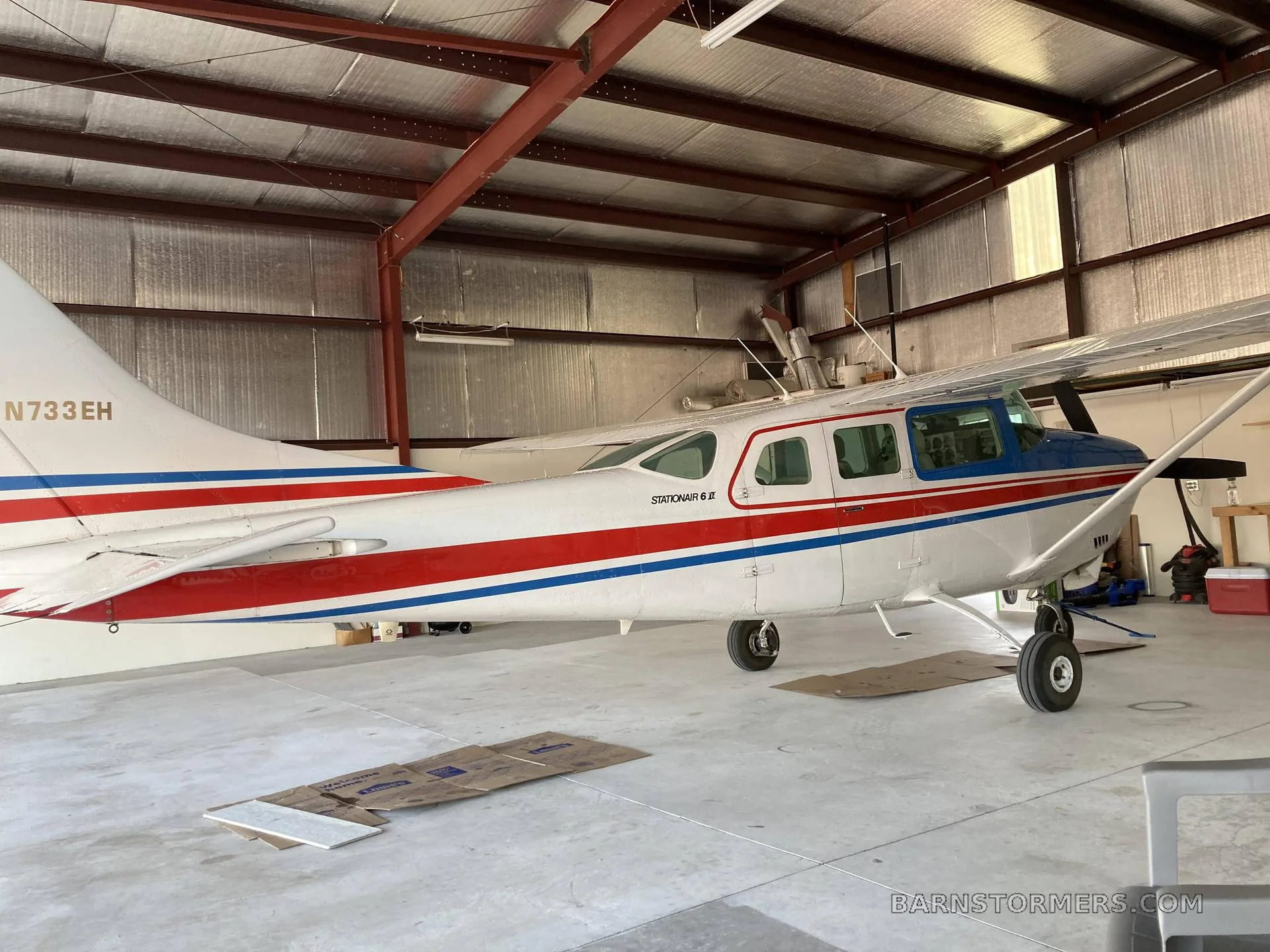 A white, red, and blue Cessna Stationair 6 II (N733EH) parked inside a hangar.