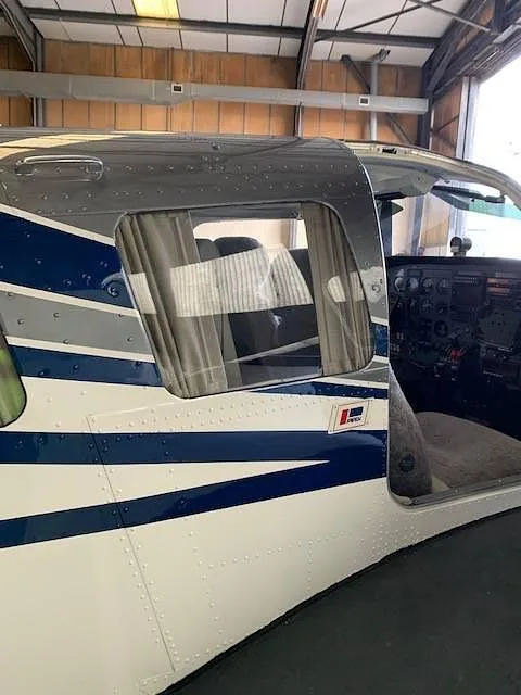 Side view of the aircraft's fuselage with an open door, revealing the cockpit and cabin interior with window curtains.