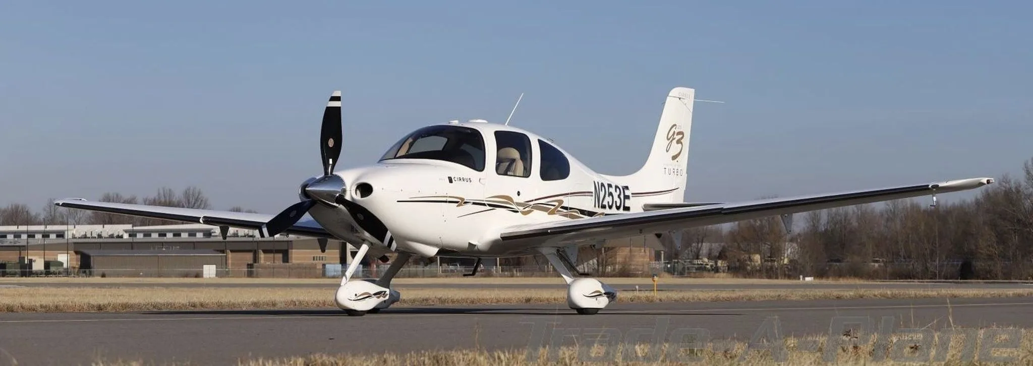 Full side view of a white Cirrus SR22T aircraft (N253E) with gold and brown stripe livery, parked on an airfield.