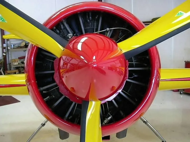A close-up front view of the red and yellow propeller and engine cowling of the Sukhoi Su-26 aircraft.
