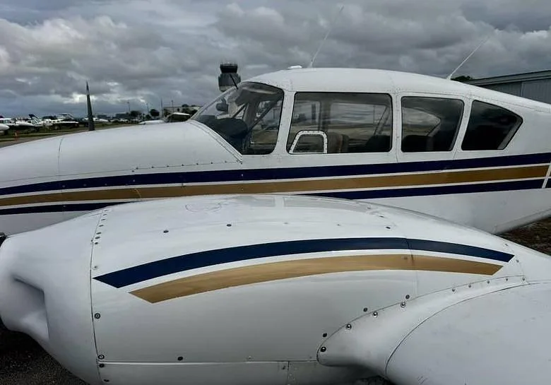 A close-up view of the white fuselage and wing of a twin-engine aircraft with blue and gold stripes, parked at an airport.