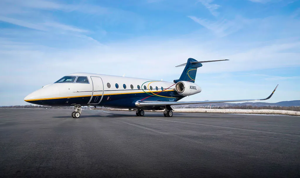 A Gulfstream G550 aircraft, registration N38GL, with a white and dark blue livery, is seen from a side view on a winter airfield.
