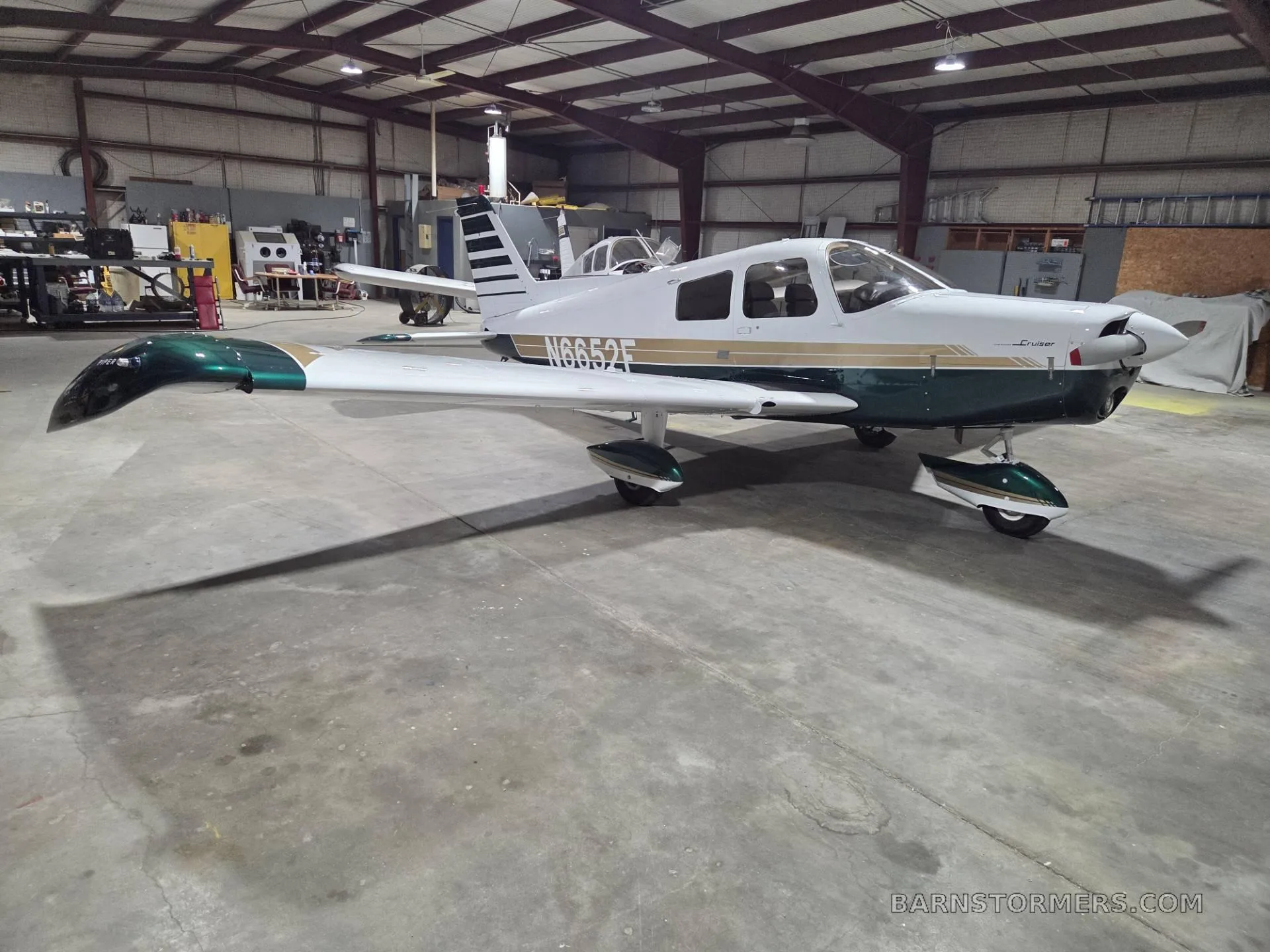 A white and green single-engine propeller aircraft (N6652F) is parked inside a hangar, viewed from the front left.