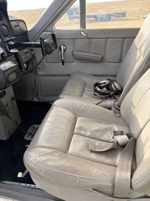 The light gray leather front seats and side panel of the aircraft interior, with a headset on the right seat.