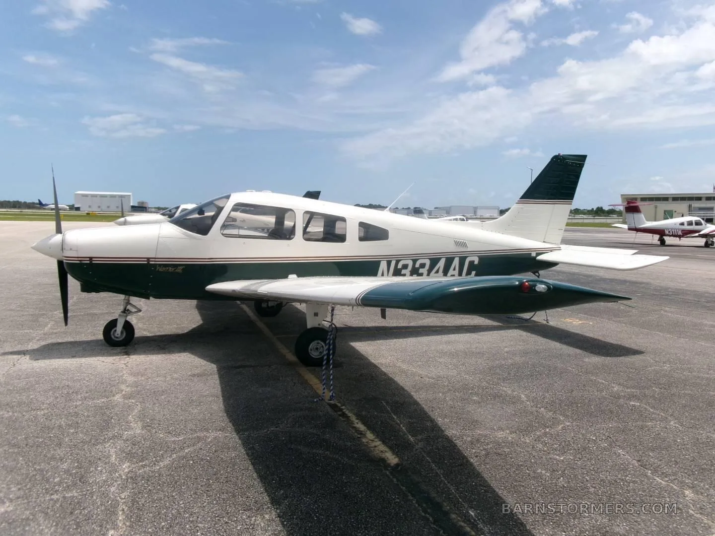 A white and dark green Piper Archer II (N334AC) parked on an asphalt ramp under a partly cloudy sky.
