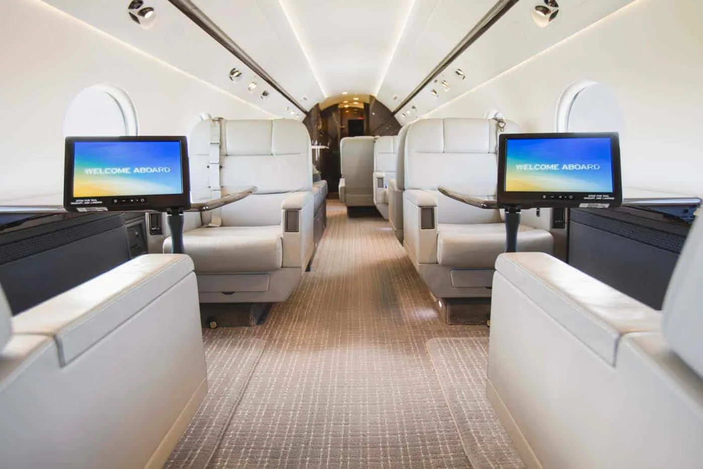 A luxurious aircraft cabin with light-colored seats and individual entertainment screens displaying "WELCOME ABOARD".