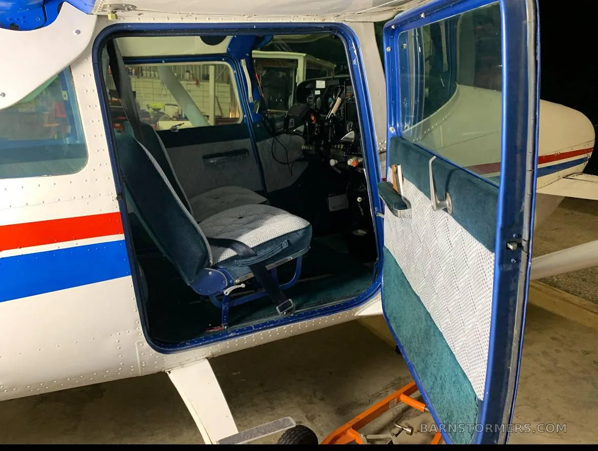 The open door of a small aircraft revealing the blue and gray interior with front and rear seats.