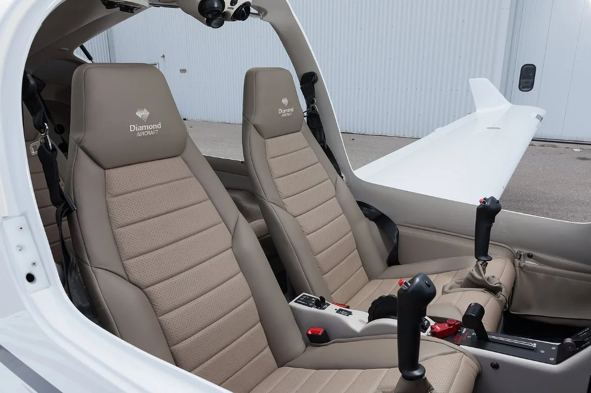 The tan leather front seats and central console of a Diamond aircraft, with the tail visible outside.