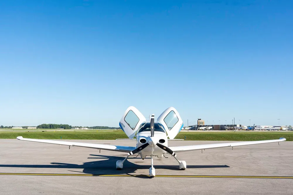 A wide front view of the white Cirrus SR22 aircraft with its gull-wing doors open, parked on an airfield.