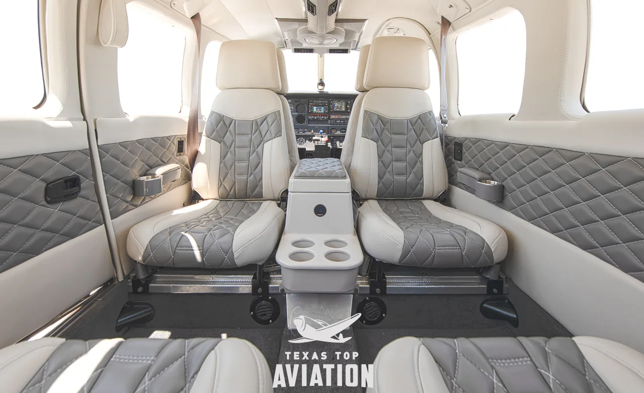 A view of the aircraft's interior cabin looking forward, showing two rows of white and grey quilted seats and a center console.