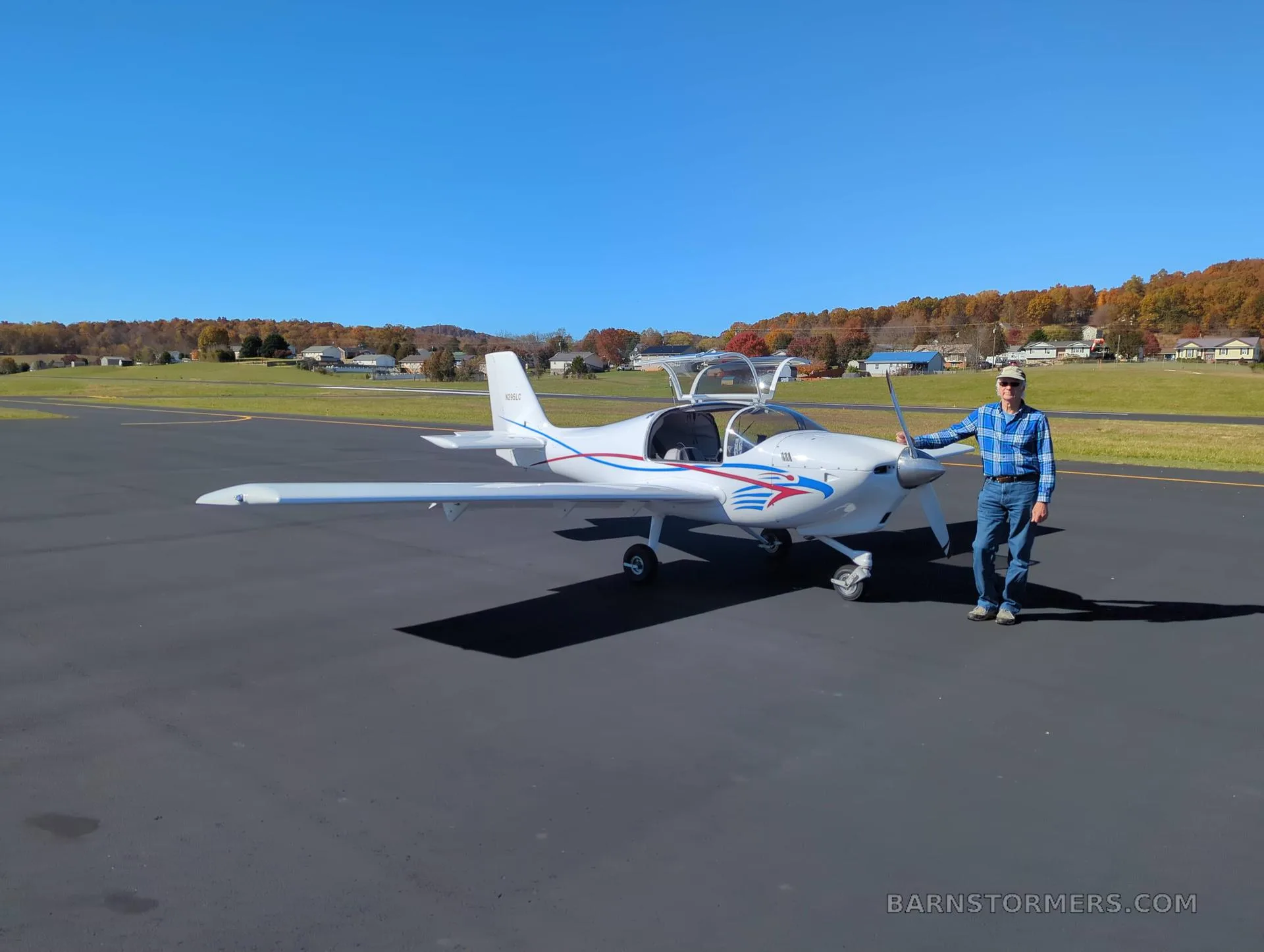 A white Europa aircraft with red and blue stripes on an airfield, with a man standing next to the propeller.