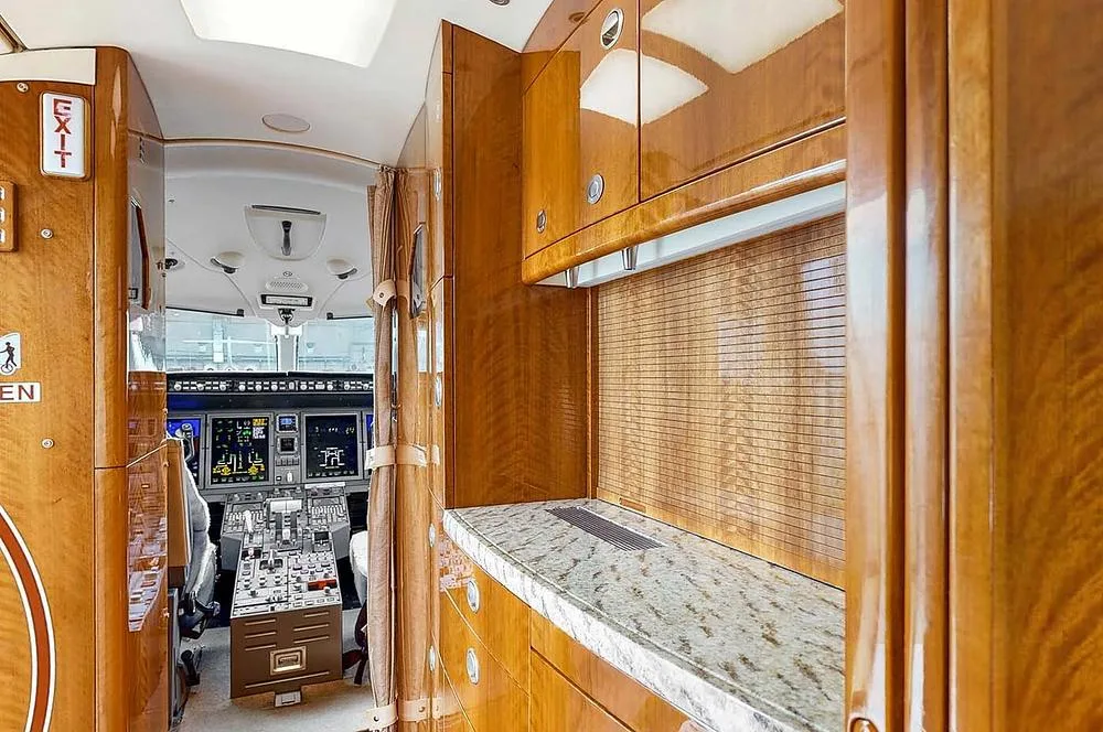 The aircraft galley area with wood cabinetry and a granite countertop, looking into the cockpit.