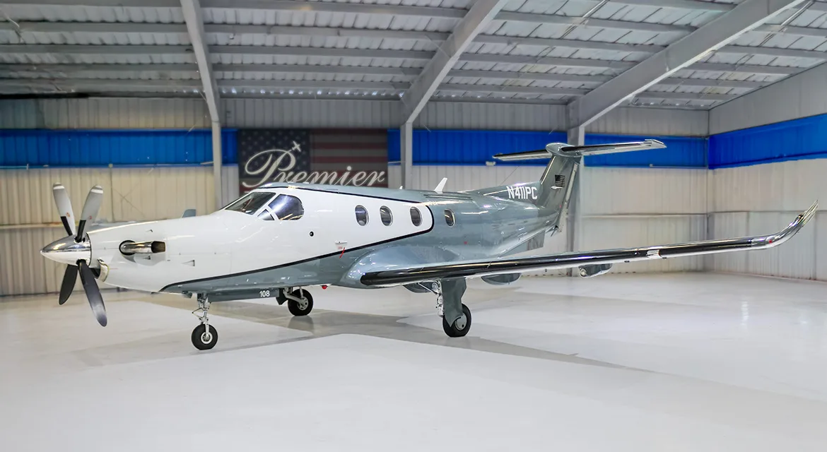 A white and grey Pilatus PC-12 turboprop aircraft, tail number N411PC, parked inside a hangar.