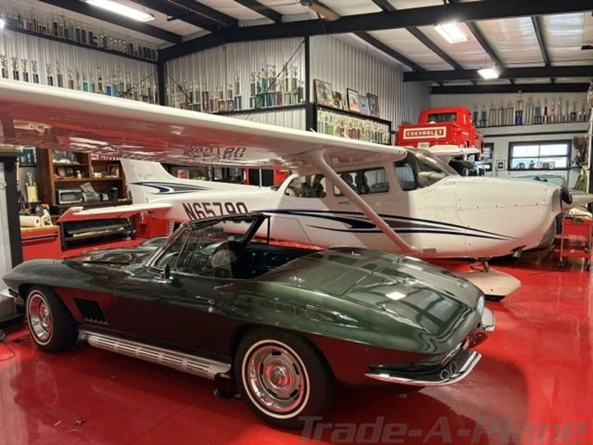 A white Cessna N65790 with blue and black stripes is parked in a hangar, with a green classic convertible car in the foreground.