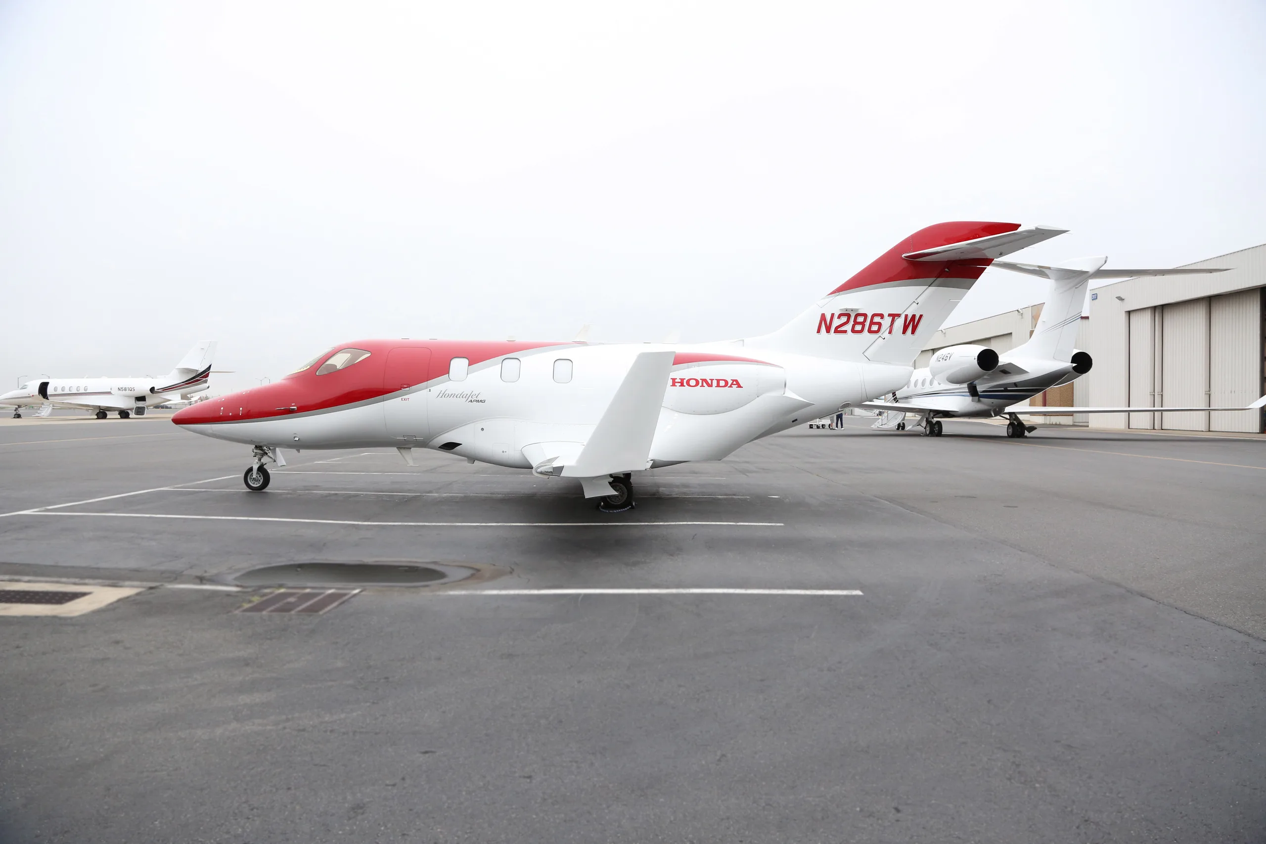 A white and red HondaJet, registration N286TW, parked on an airport tarmac with other aircraft in the background.