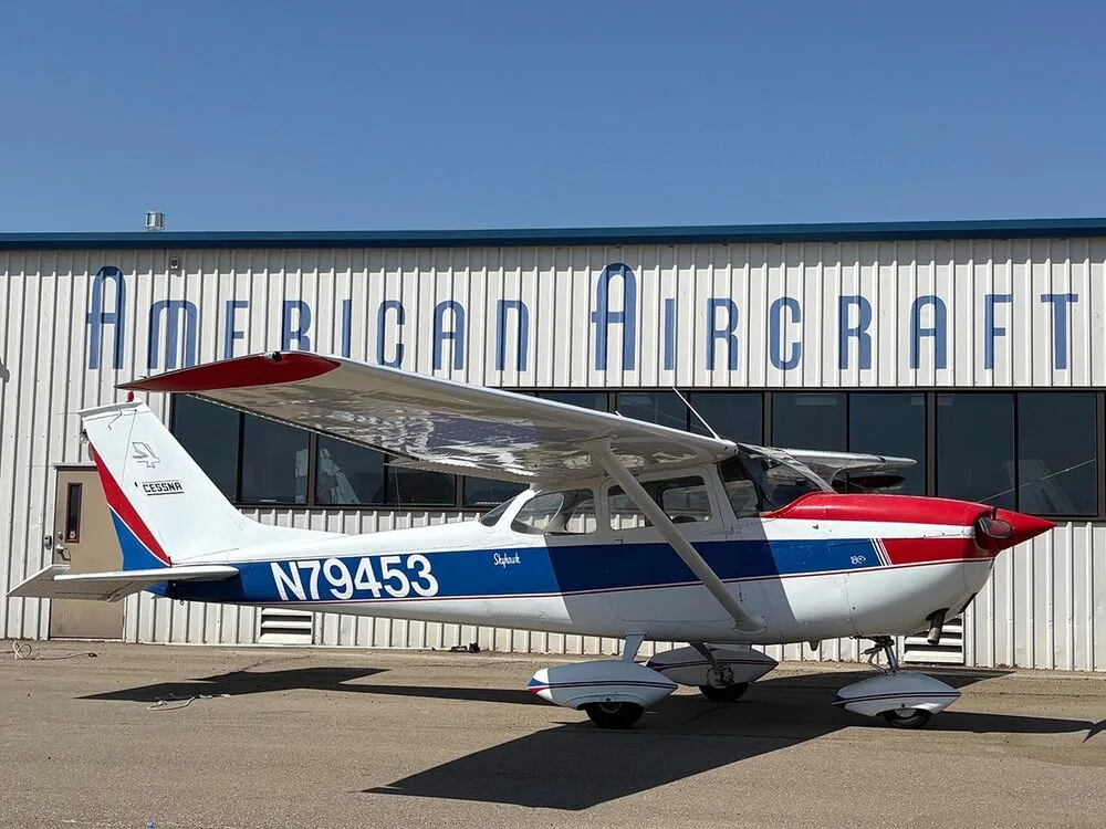 A white, red, and blue Cessna Skyhawk N79453 parked on an tarmac in front of an "AMERICAN AIRCRAFT" hangar.