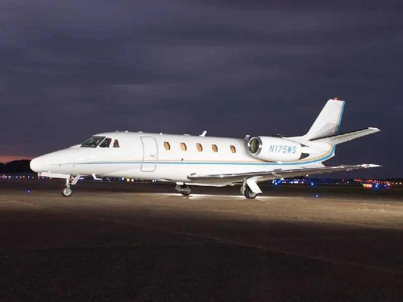 A white jet with blue and gold accents parked on the tarmac at night.