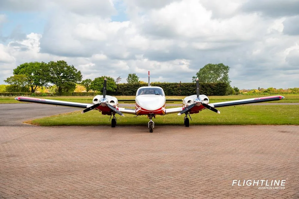 A front view of a red and white twin-engine Piper Seneca aircraft parked on a paved surface.