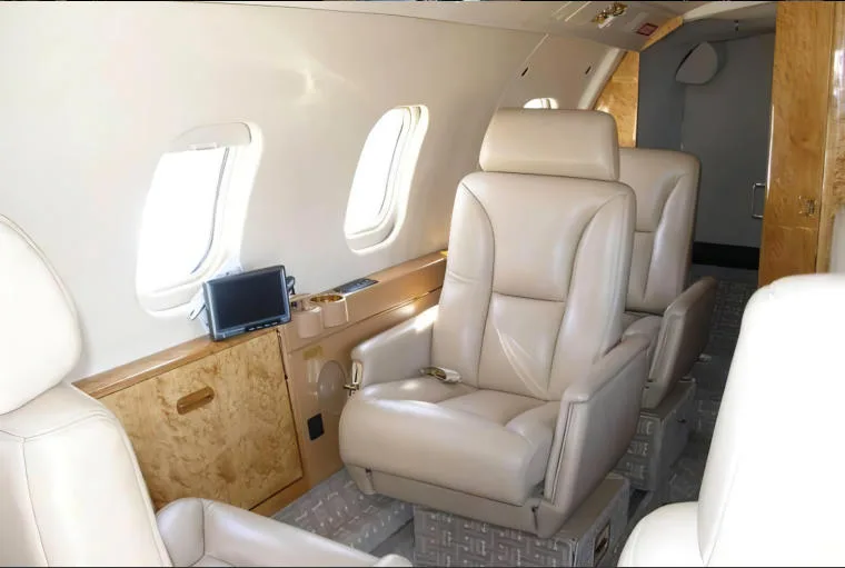 The luxurious interior cabin of a private jet with beige leather seats and polished wood accents.