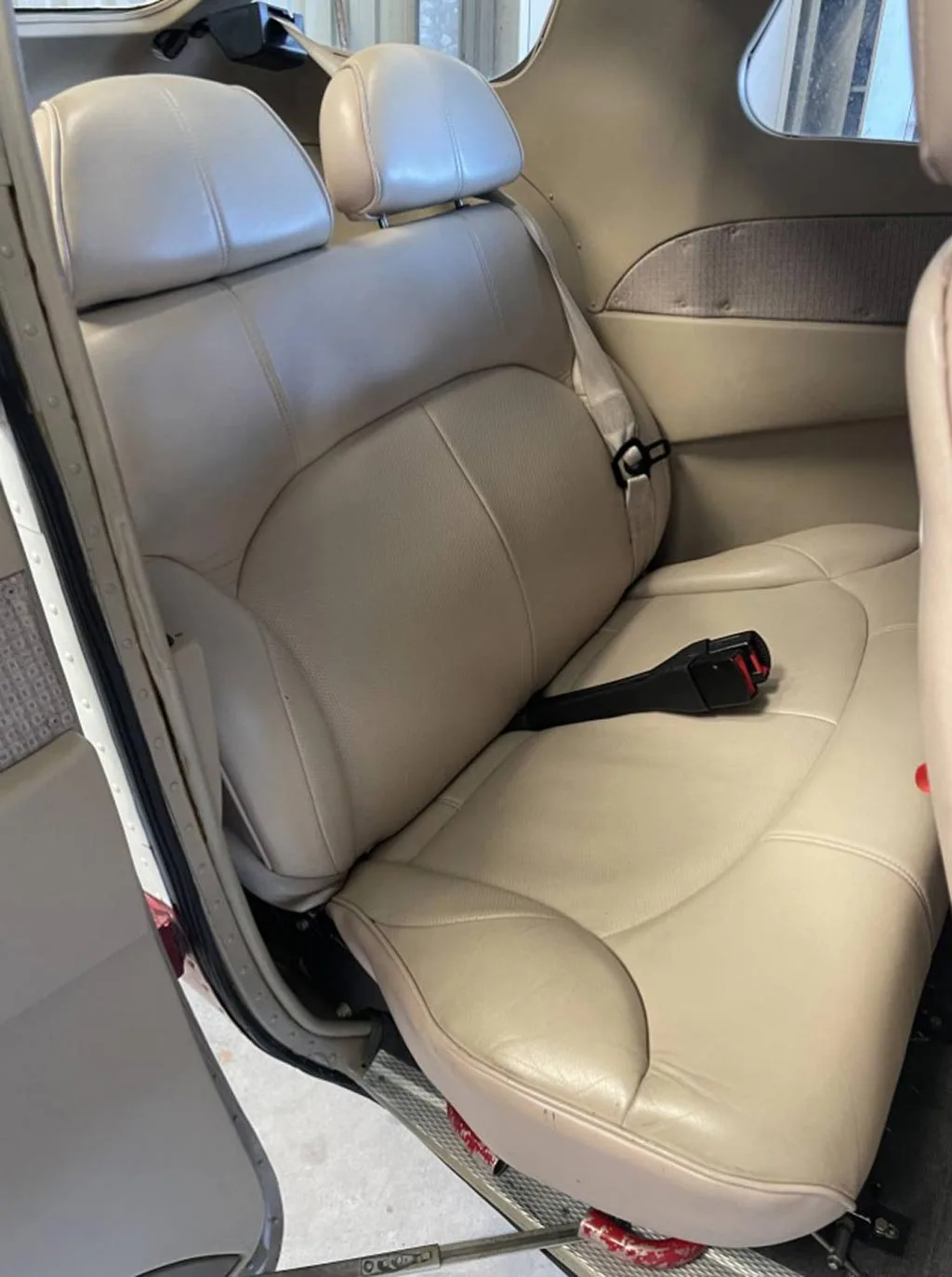 A close-up view of the beige leather rear bench seat in the aircraft cabin.