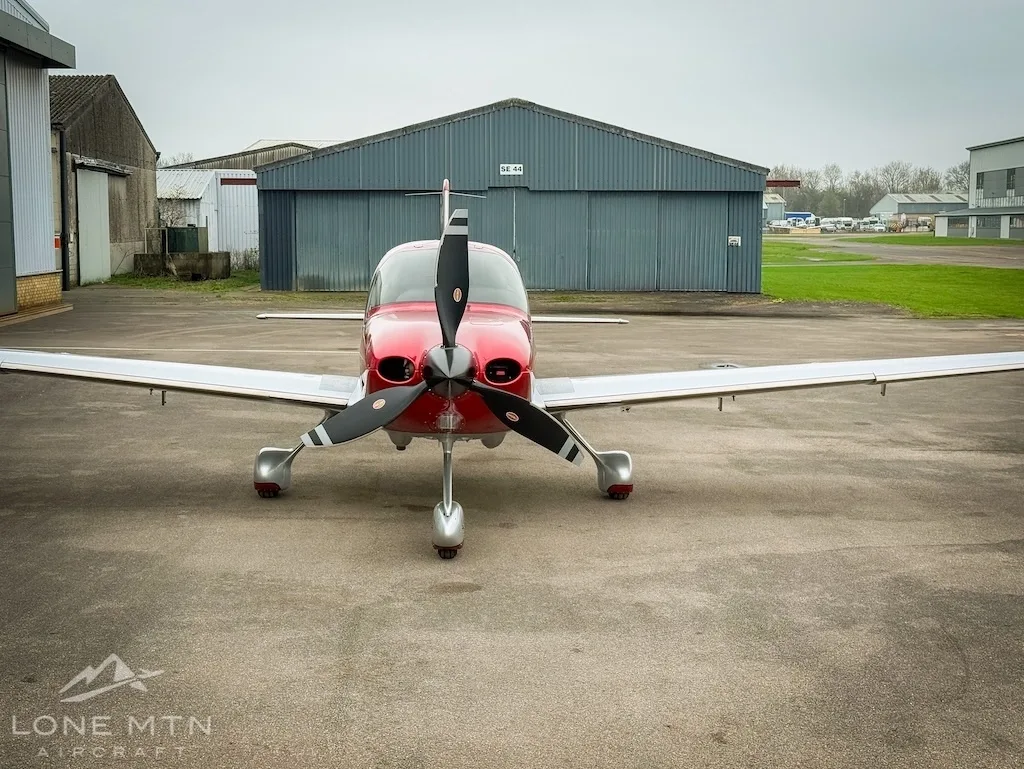 A red and white Cirrus SR22 aircraft (G-PFLY) viewed from the front on a tarmac.