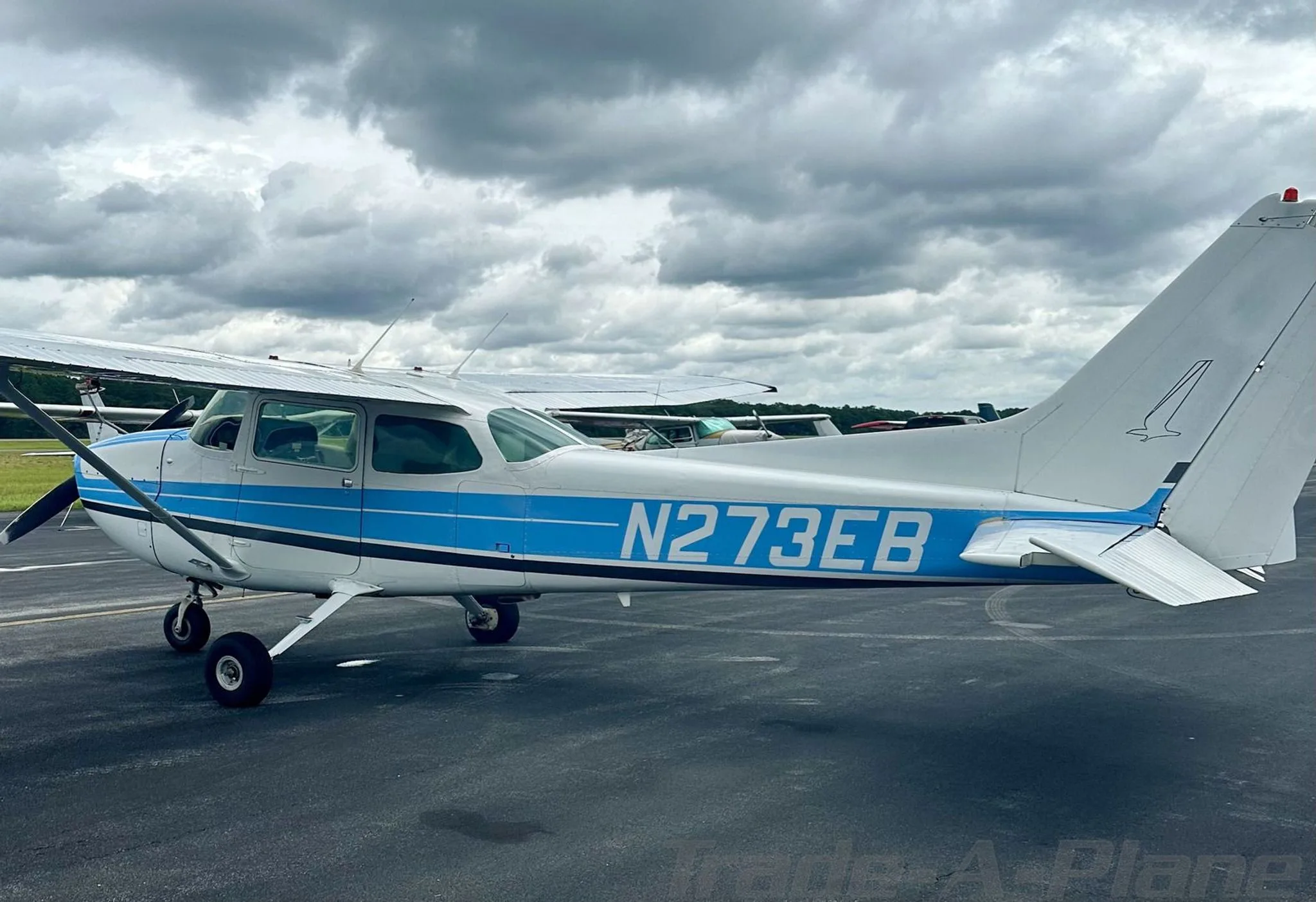 A side view of the white and blue Cessna 172, registration N273EB, on an airport tarmac.