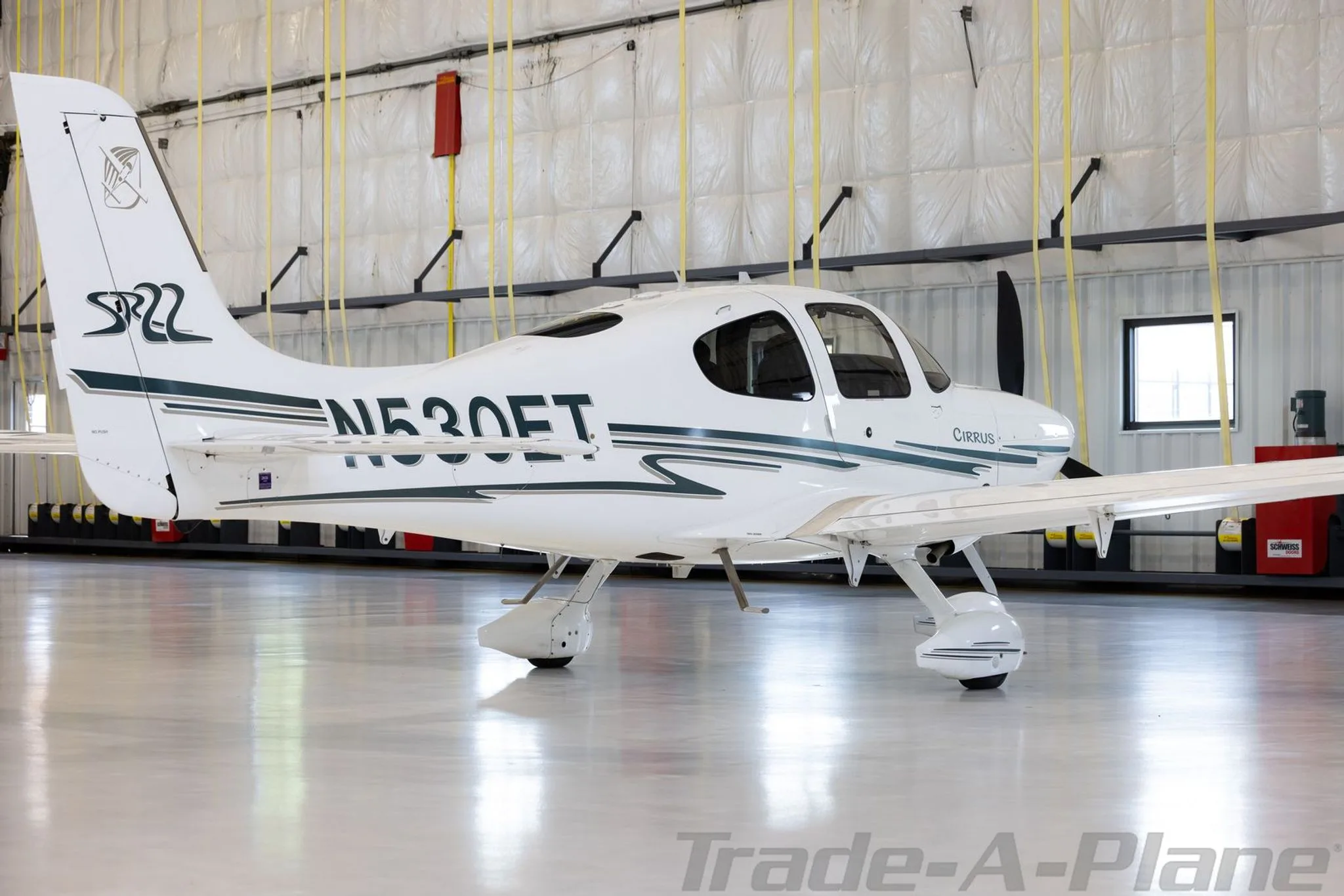 A white Cirrus SR22 aircraft with N530ET registration and green stripes is parked in a hangar, viewed from the rear right.