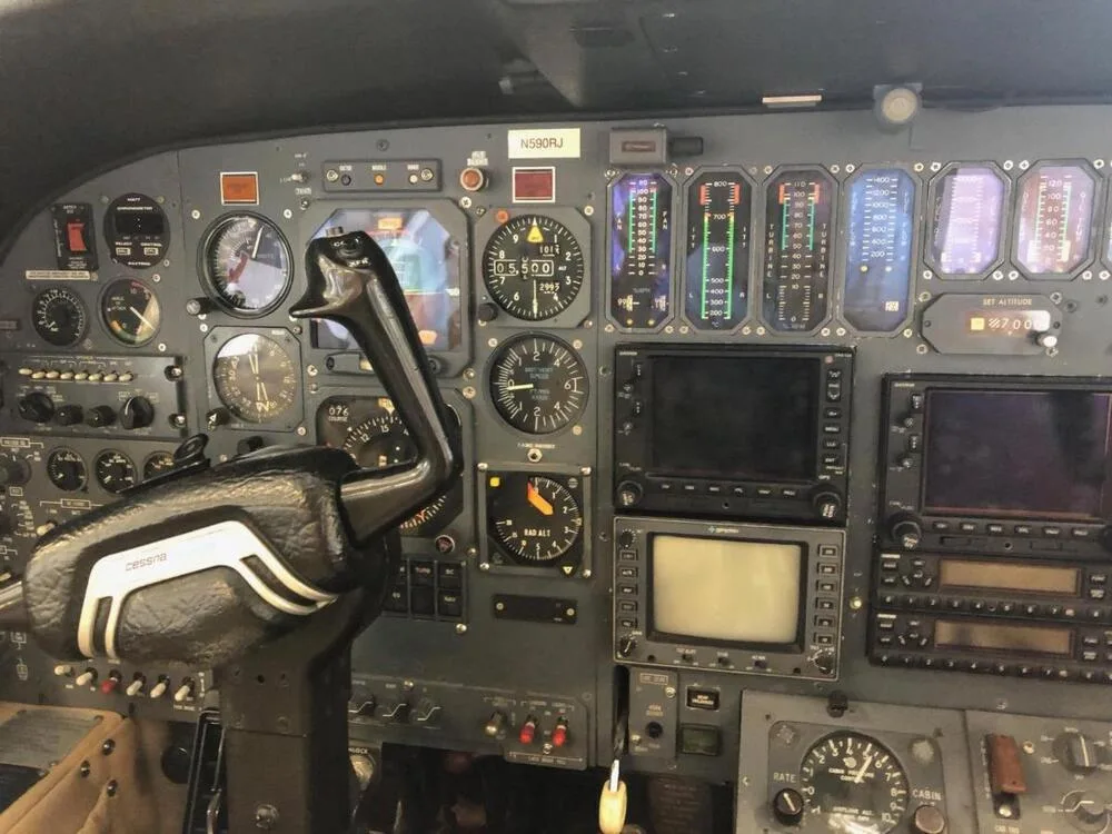 A wide view of the aircraft's cockpit instrument panel, showing various gauges, screens, and the pilot's control yoke.