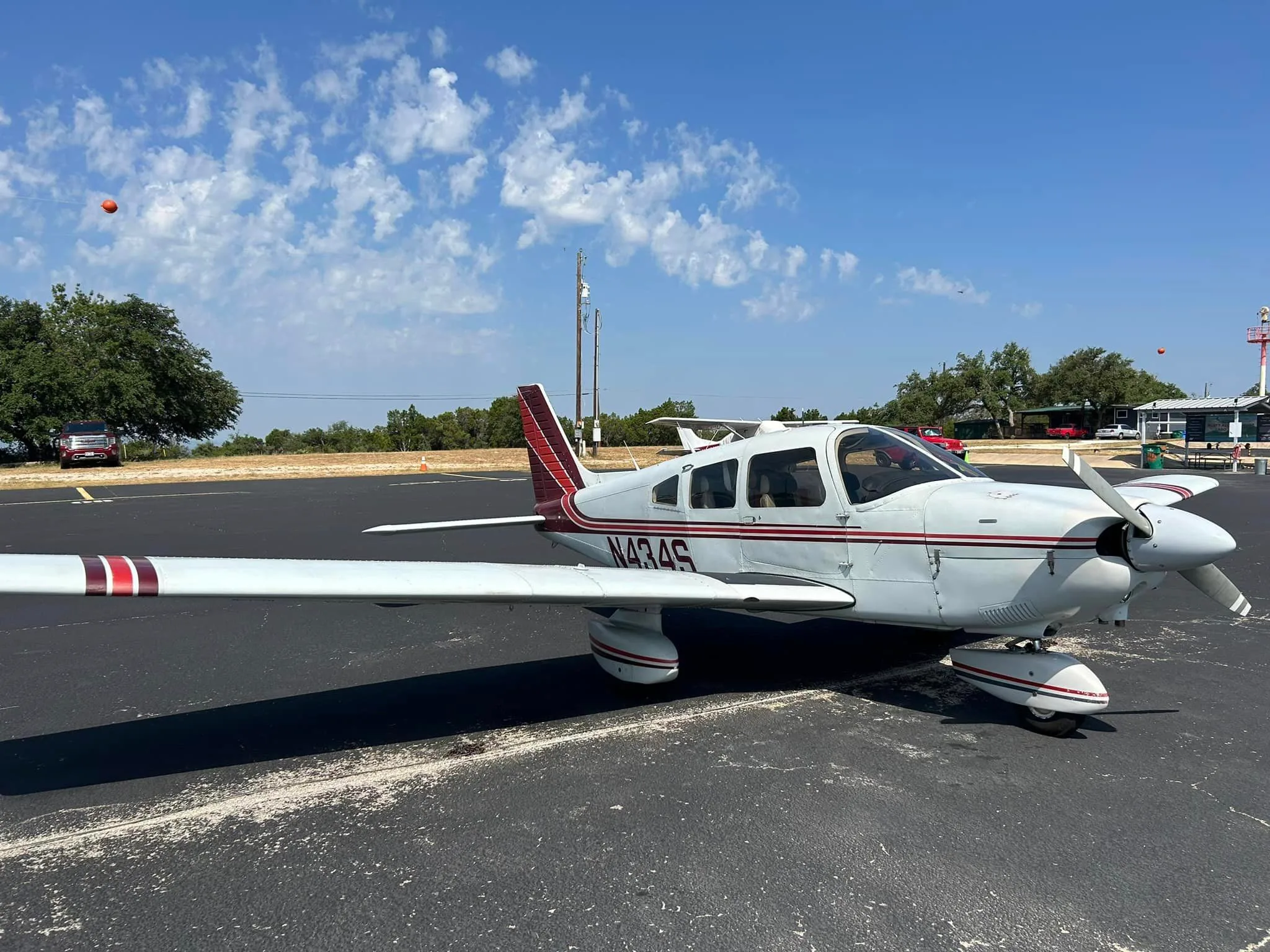 A white single-engine aircraft with red and dark stripes, tail number N434S, parked on an asphalt ramp on a sunny day.