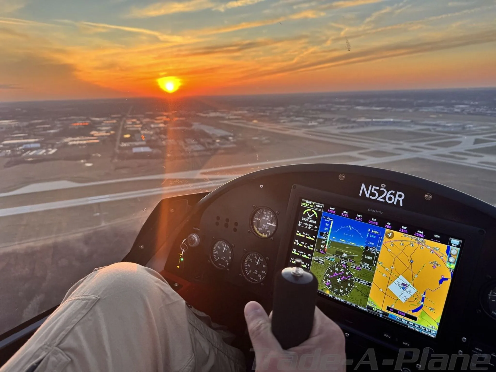 A pilot's view from the cockpit of an Air-Cam, showing the instrument panel with a Garmin G3X Touch display and a sunset over an airport.