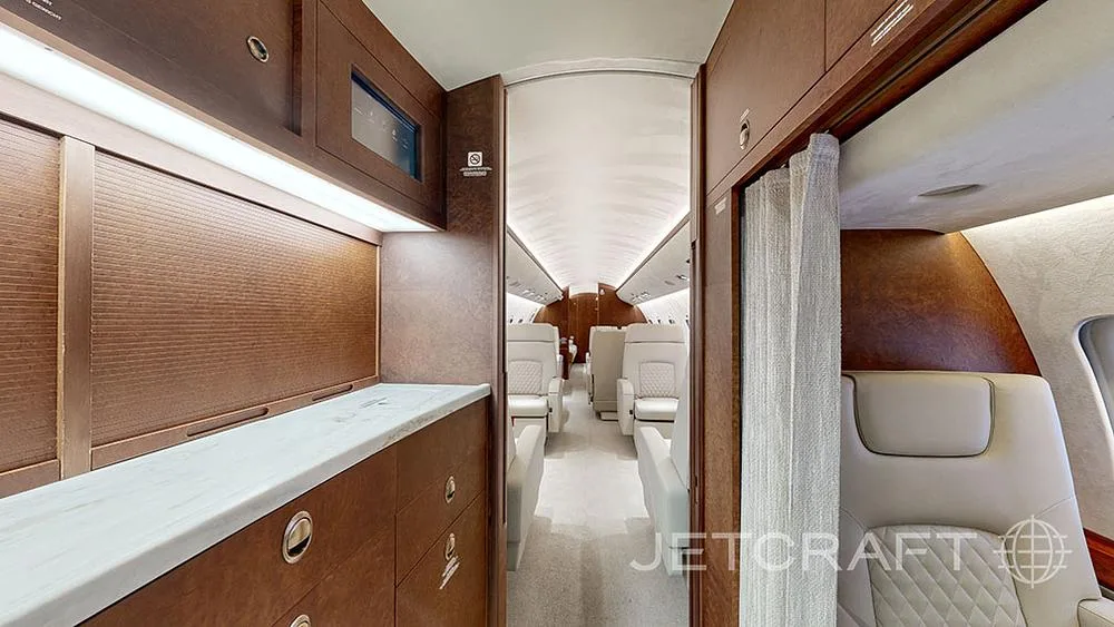 A view of the aircraft's galley area with wooden cabinetry and a marble-like countertop, looking into the main cabin.