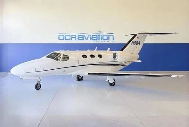 A white Cessna Citation private jet, registration N9BA, is parked in a hangar with a blue and white wall.