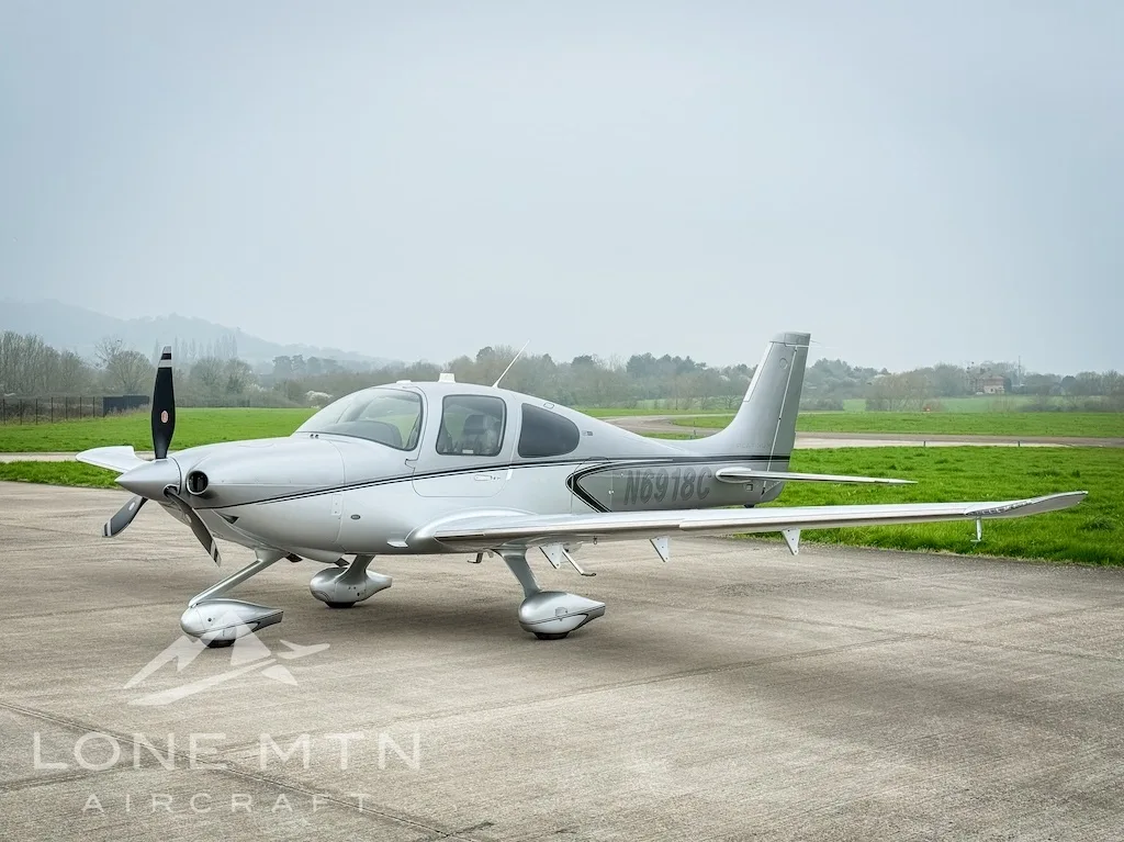 A silver Cirrus SR22 aircraft, registration N6918C, parked on an airfield on a cloudy day.