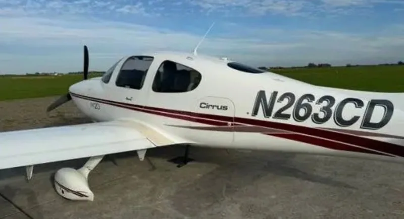 A white Cirrus SR20 aircraft with registration N263CD and a red stripe, viewed from the left side on a tarmac.