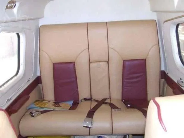 Two tan and maroon aircraft passenger seats with seatbelts and windows on either side.