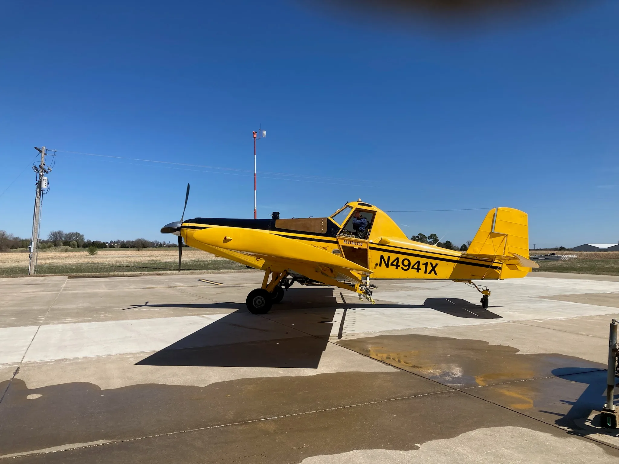 A yellow and black crop duster aircraft, N4941X, parked on a concrete pad under a clear blue sky.
