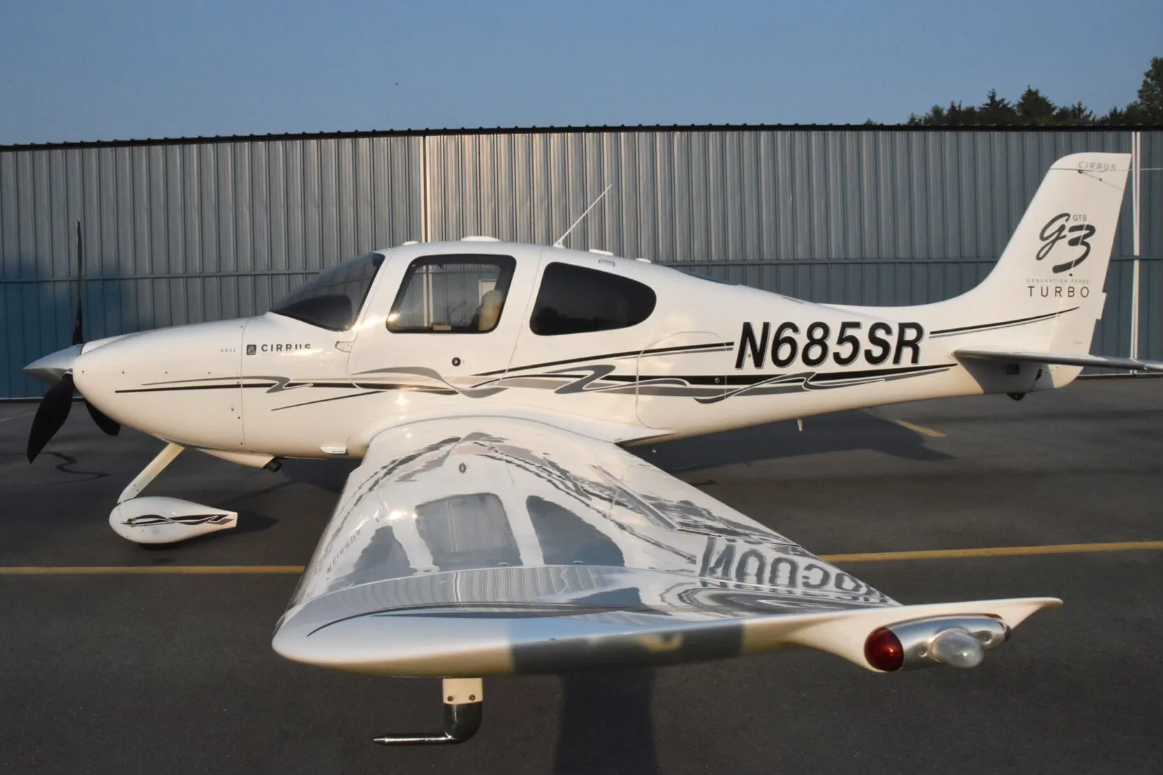 A rear-quarter view of the white Cirrus SR22T aircraft (N685SR) showing the reflective underside of the wing.