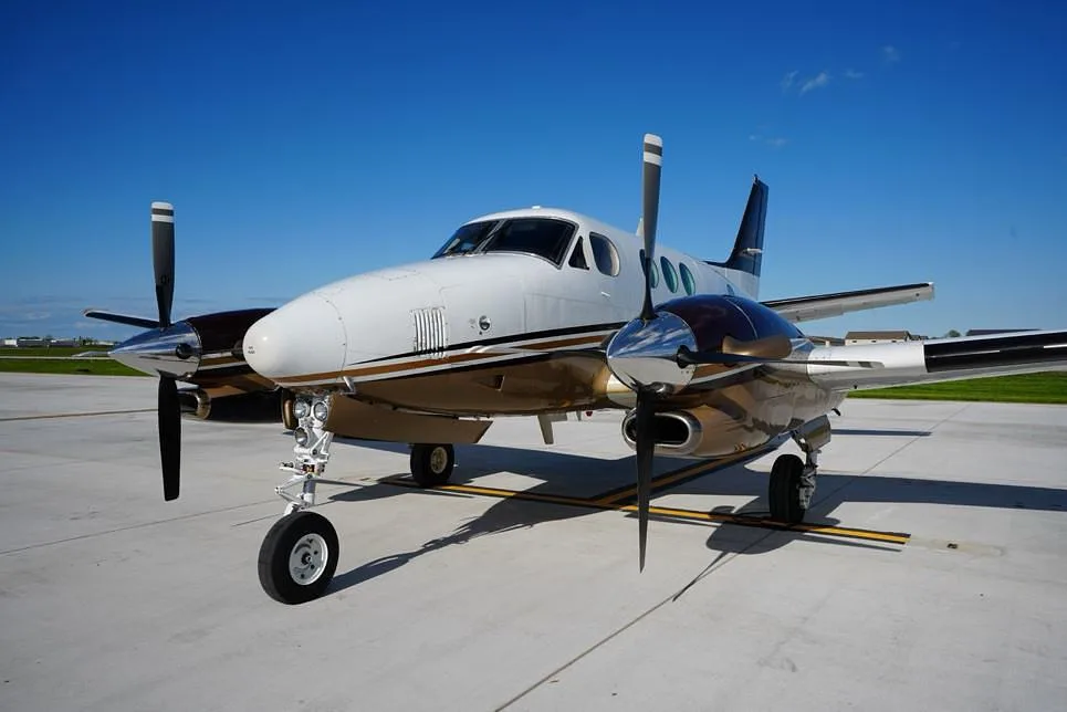 A front-quarter view of a white and brown Beechcraft King Air 200 parked on an airfield.