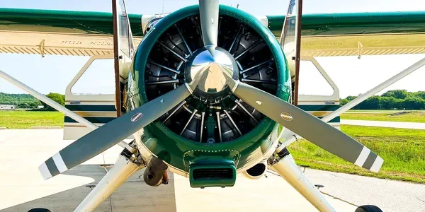 Front view of a green and white single-engine aircraft with a large propeller on an airfield.