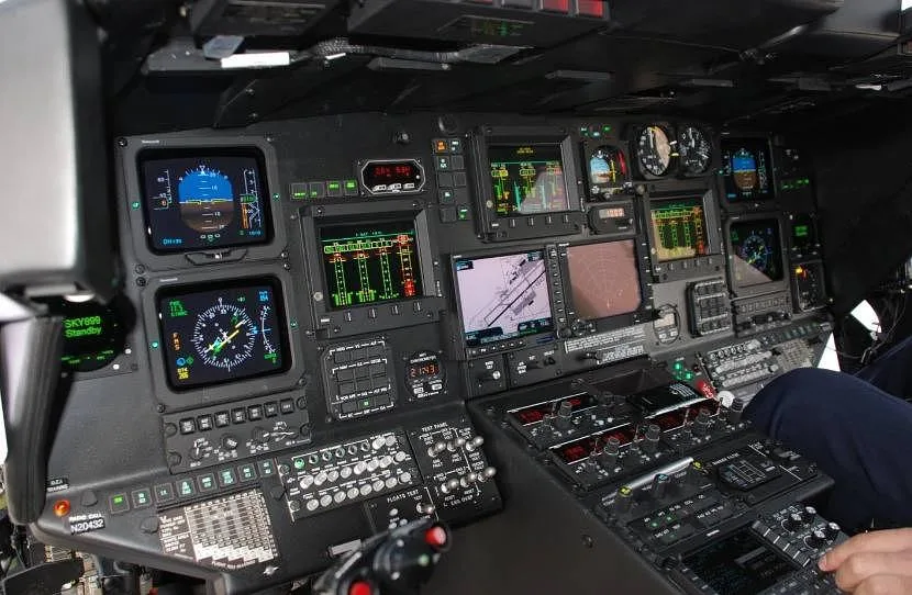 A modern helicopter cockpit with multiple digital displays, gauges, and control panels.