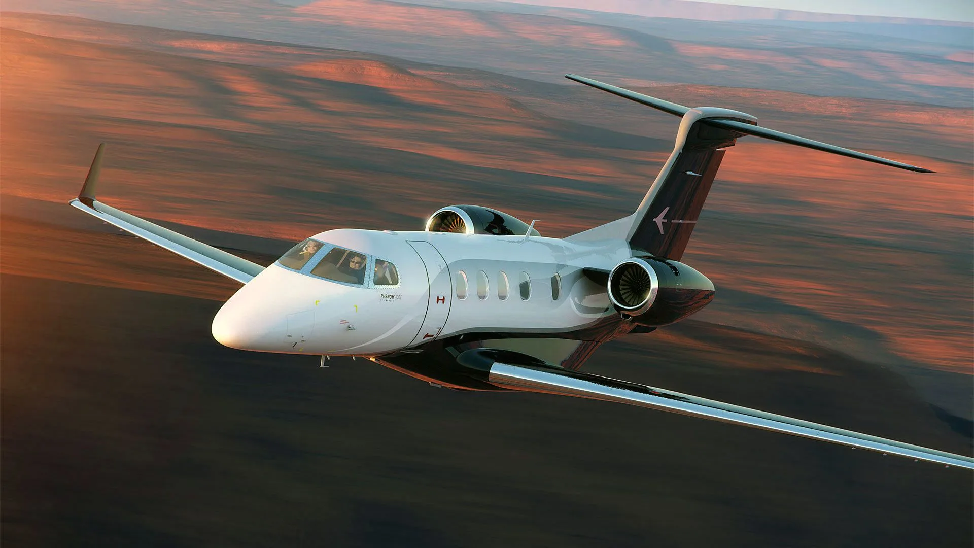 A Phenom 300E business jet in flight over a desert landscape.