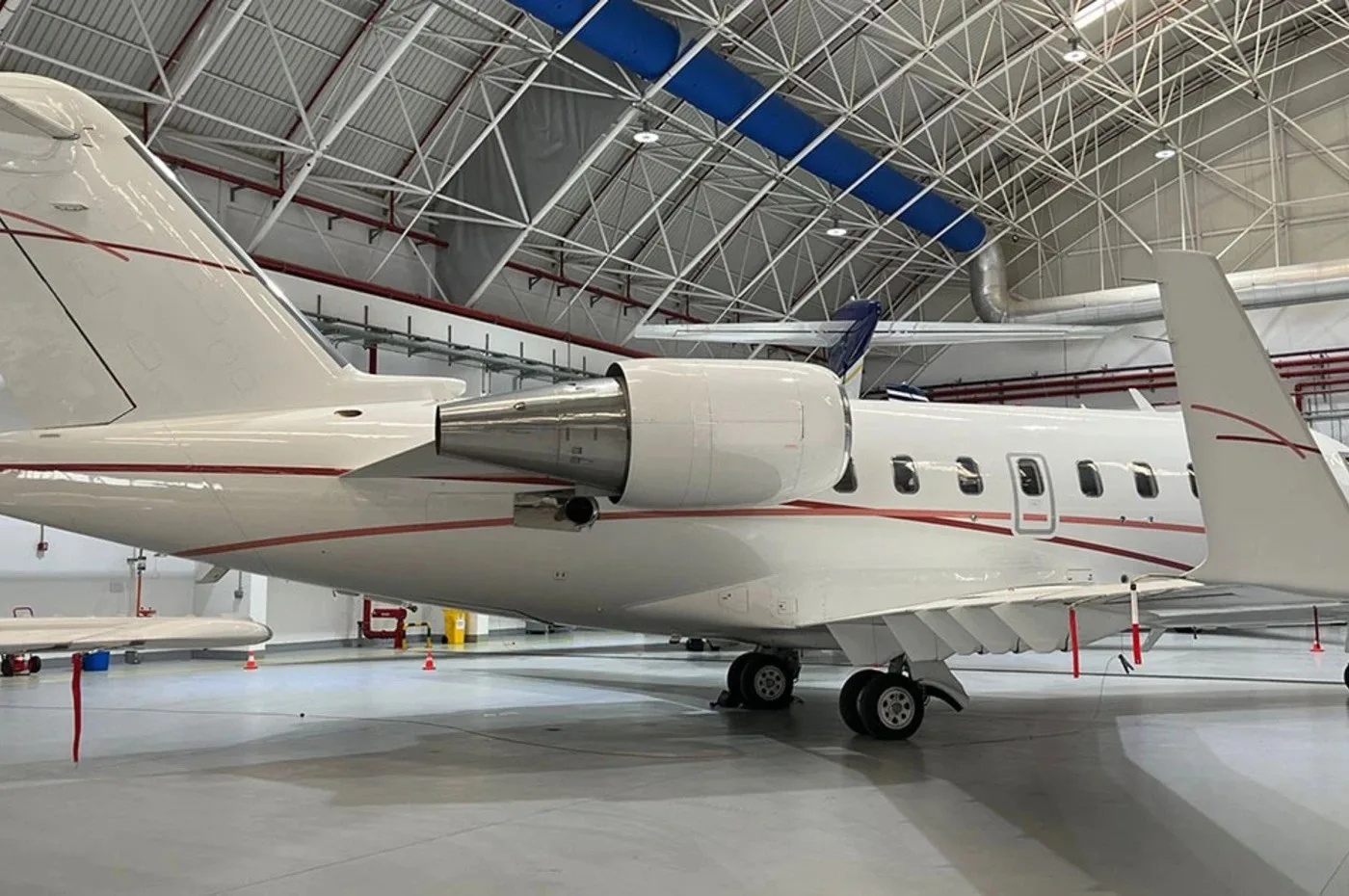A white business jet with red pinstripes parked inside a hangar, viewed from the rear-right.