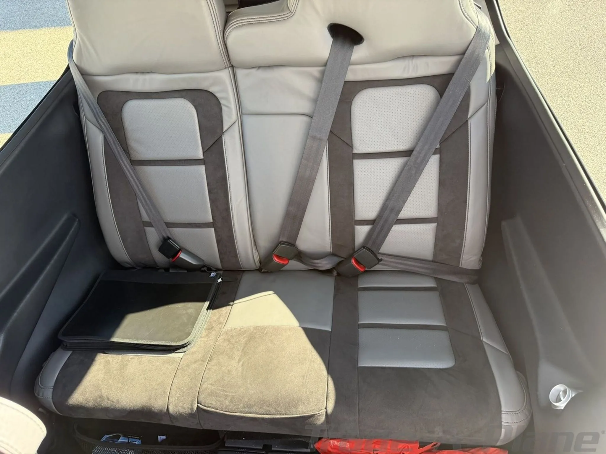 The grey and dark grey leather rear seats of the aircraft cabin with seatbelts fastened.