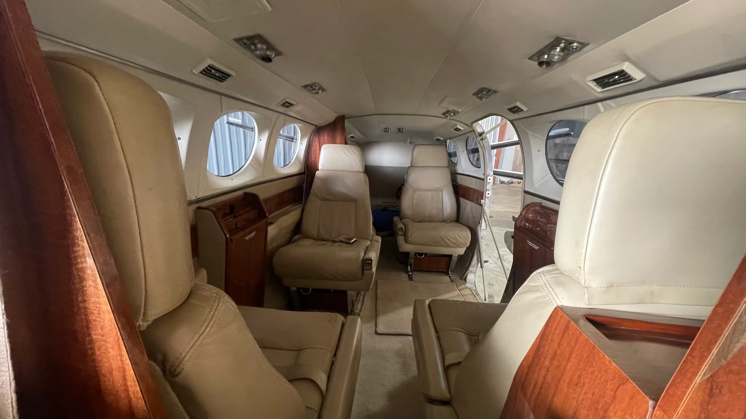 View of the aircraft's tan leather passenger cabin with four seats and wood trim.
