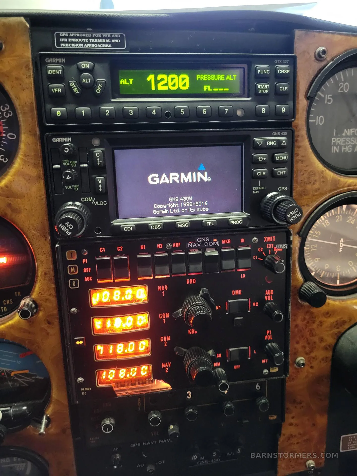 A close-up of an aircraft's instrument panel, featuring Garmin avionics and other gauges set in a wood-grain panel.
