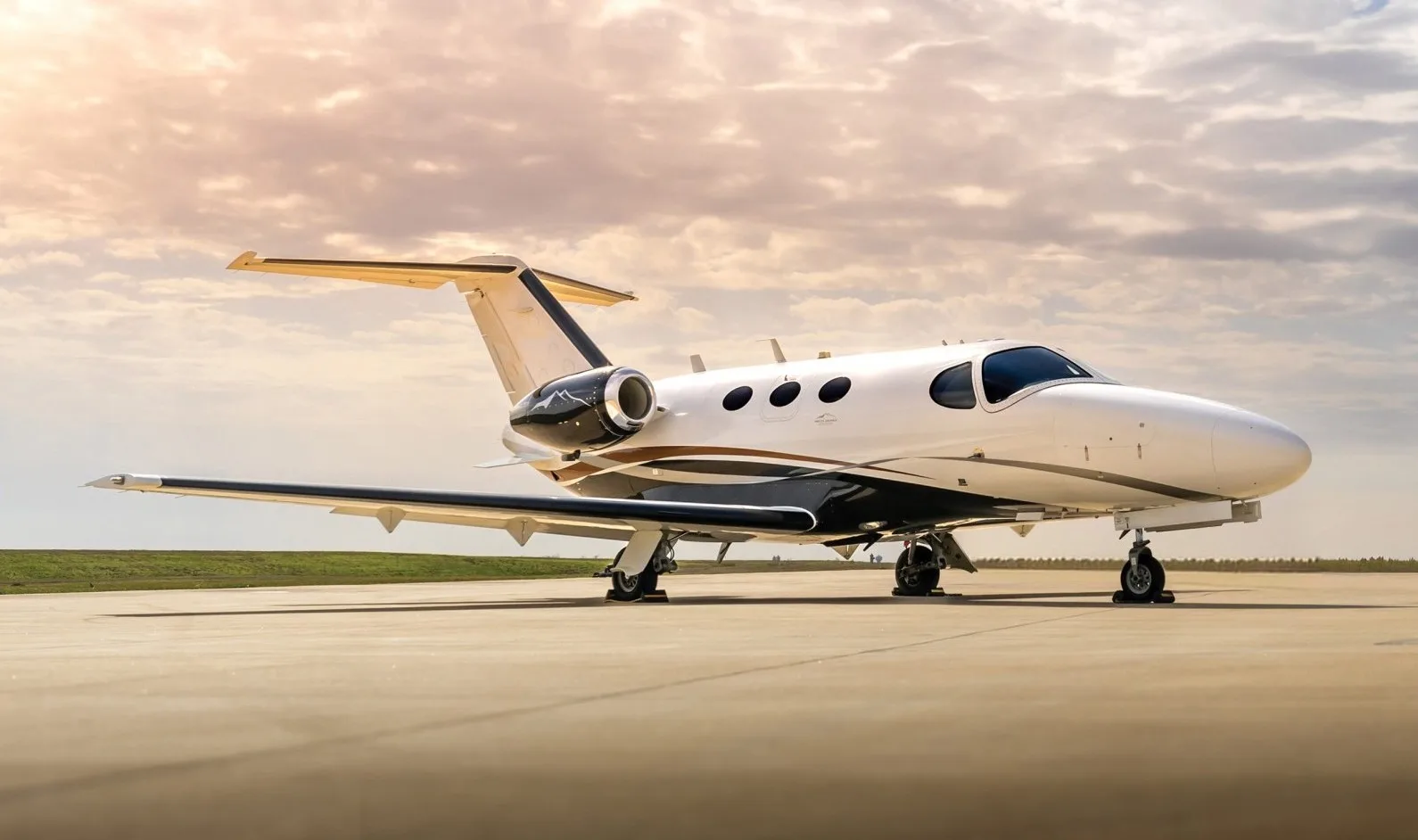 A white and black Cessna Citation business jet is parked on an airport tarmac under a cloudy, golden sunset sky.