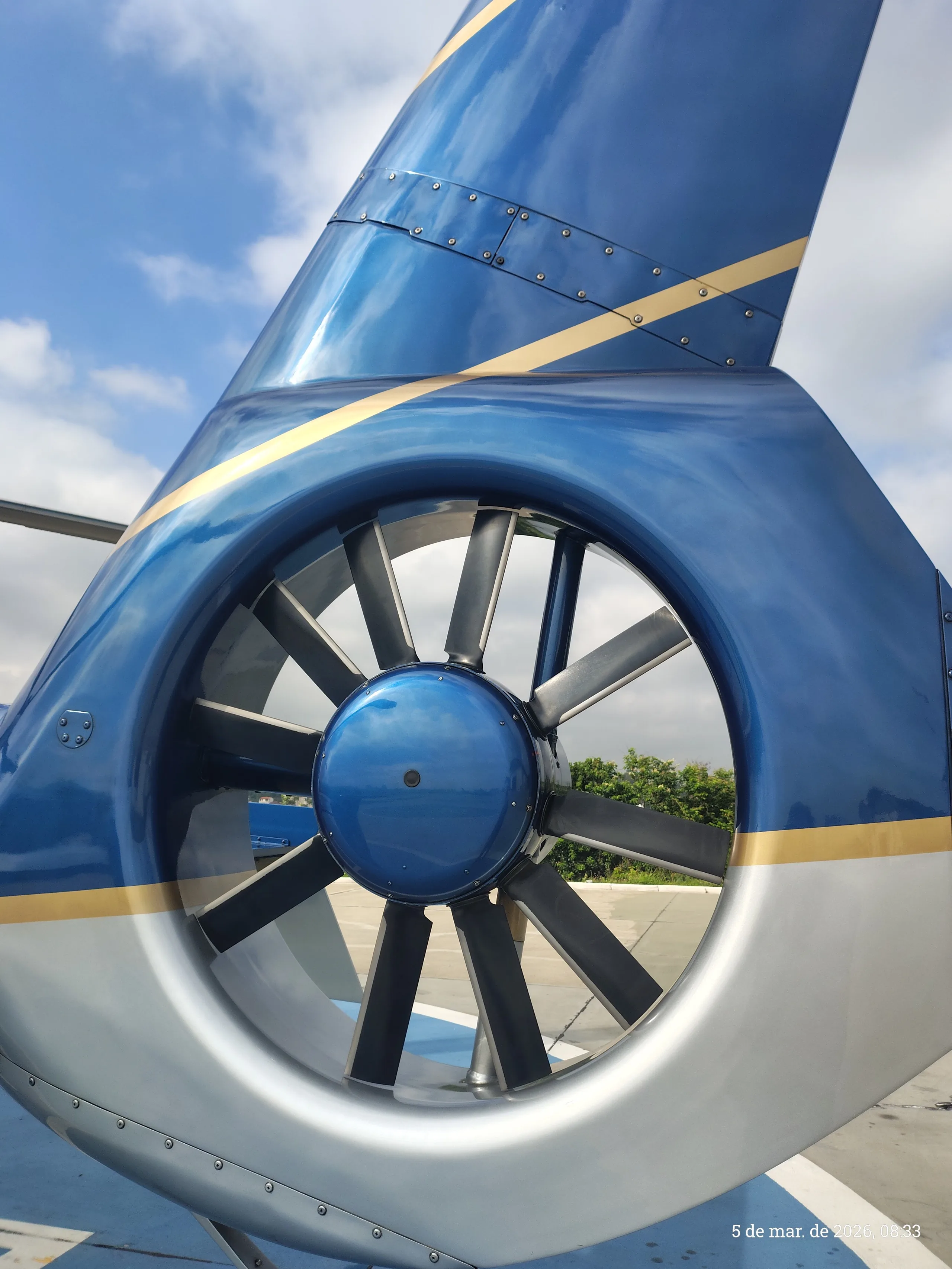 A close-up view of the blue and silver helicopter's tail rotor (fenestron) with gold stripes.