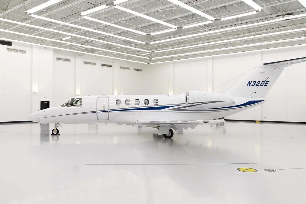 A white business jet with blue and grey stripes, registration N32GE, parked in a brightly lit hangar.